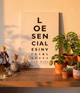 Cuadro decorativo inspirado en El Principito con frase “Lo esencial es invisible para los ojos” sobre pared blanca con decoración minimalista y plantas