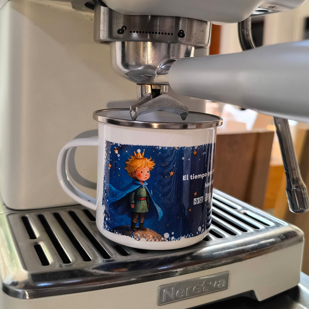 Pocillo de peltre de El Principito ubicado debajo del portafiltros de una máquina de espresso blanca.